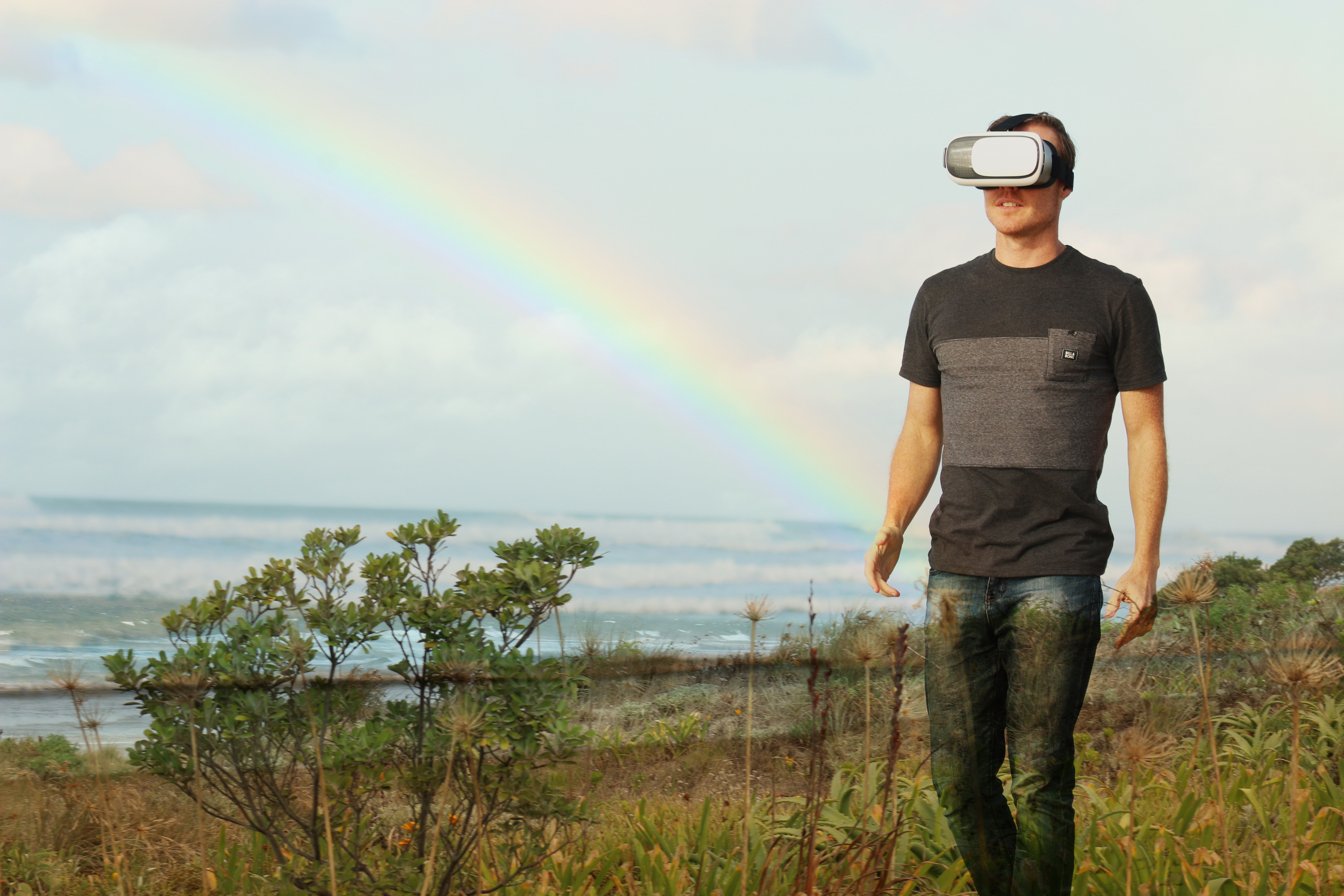 Hombre con visor de realidad virtual caminando por campo con arcoiris